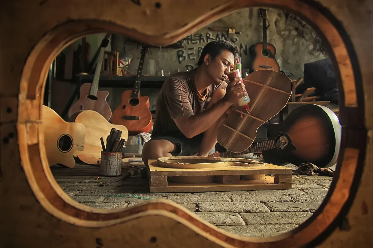 Artisan assemblant une guitare dans un atelier rempli d’instruments.