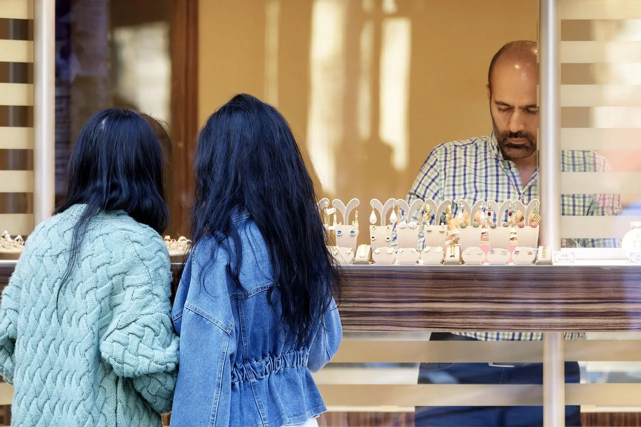 Deux clientes devant une vitrine de bijoux, avec un commerçant derrière le comptoir.
