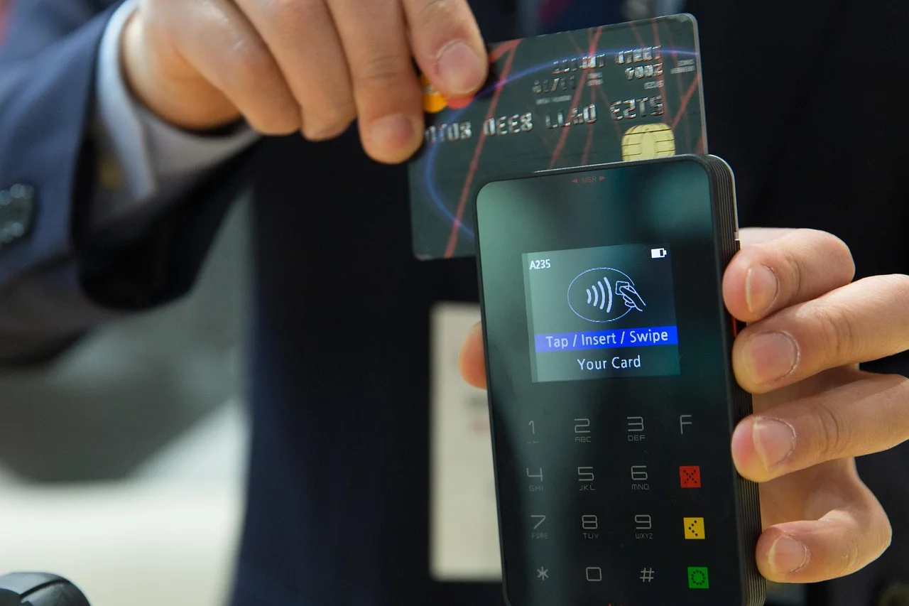 Gros plan sur une carte bancaire présentée au-dessus d’un terminal de paiement tenu en main.